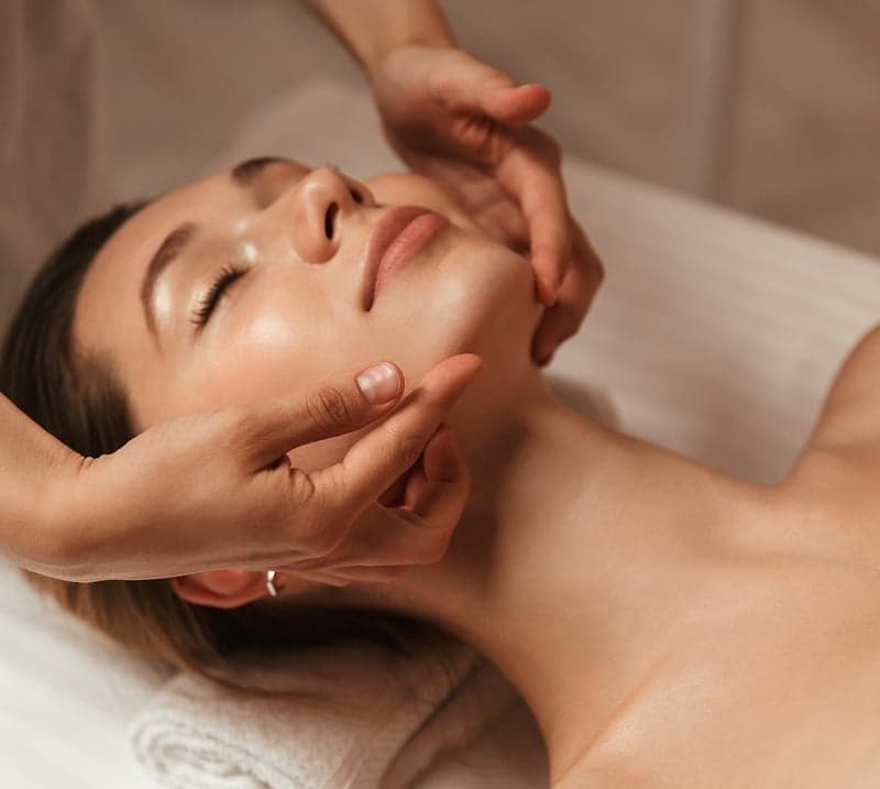 Woman getting a face massage while lying on a bed
